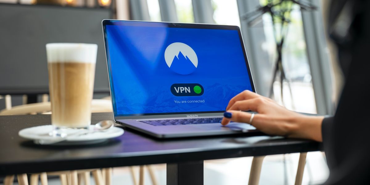 شخصی در حال تایپ با لپ‌تاپ روی میز قهوه‌خوری نشسته است.  لپ تاپ در حال اتصال به VPN است.