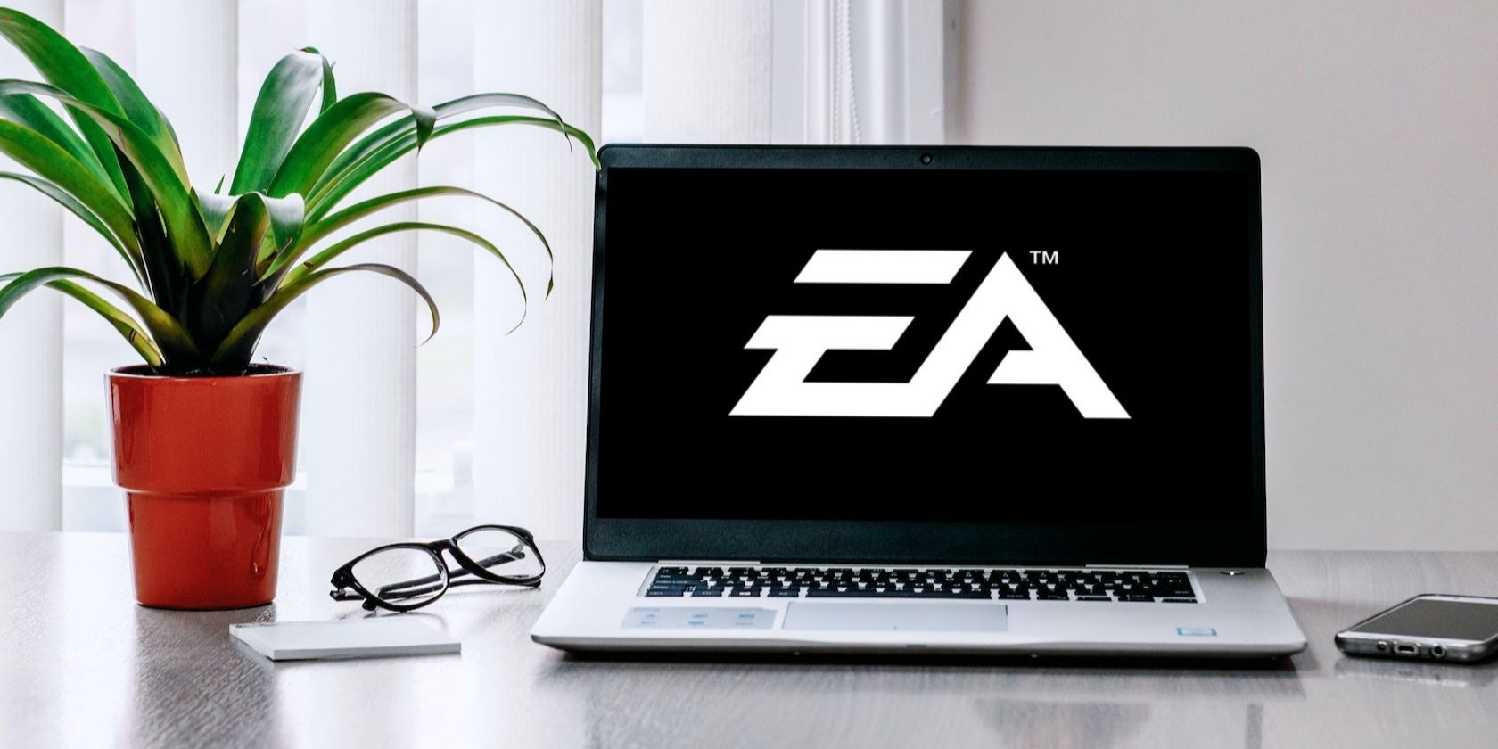DELL Laptop on the Grey Table Near the Flower and Glasses With EA Logo on Its Screen